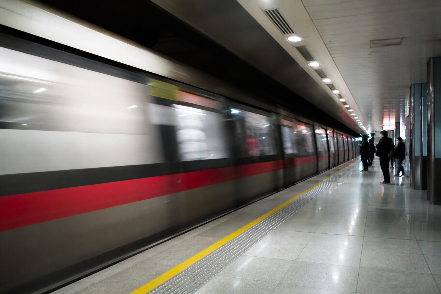 Train arriving at a platform with commuters standing behind the yellow line